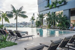 Ein Poolbereich auf dem Dach mit Liegestühlen, Palmen und Blick auf die Skyline der Stadt.