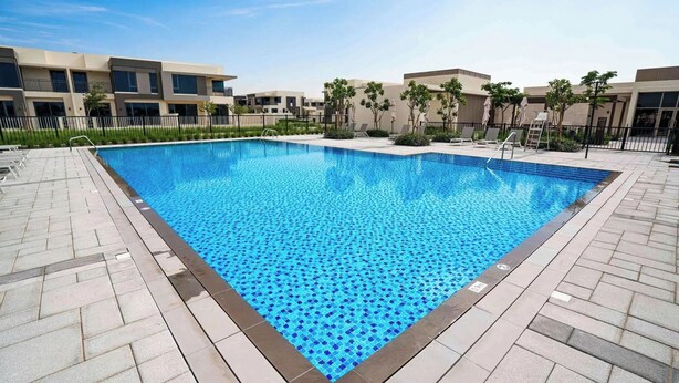 Ein rechteckiger Pool mit blauem Mosaikfliesenmuster, umgeben von einer gefliesten Terrasse und einem niedrigen Zaun.