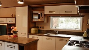 Cocina compacta con microondas, fregadero y estufa. Hay una ventana que proporciona luz natural y una pequeña encimera con un cuenco de fruta.