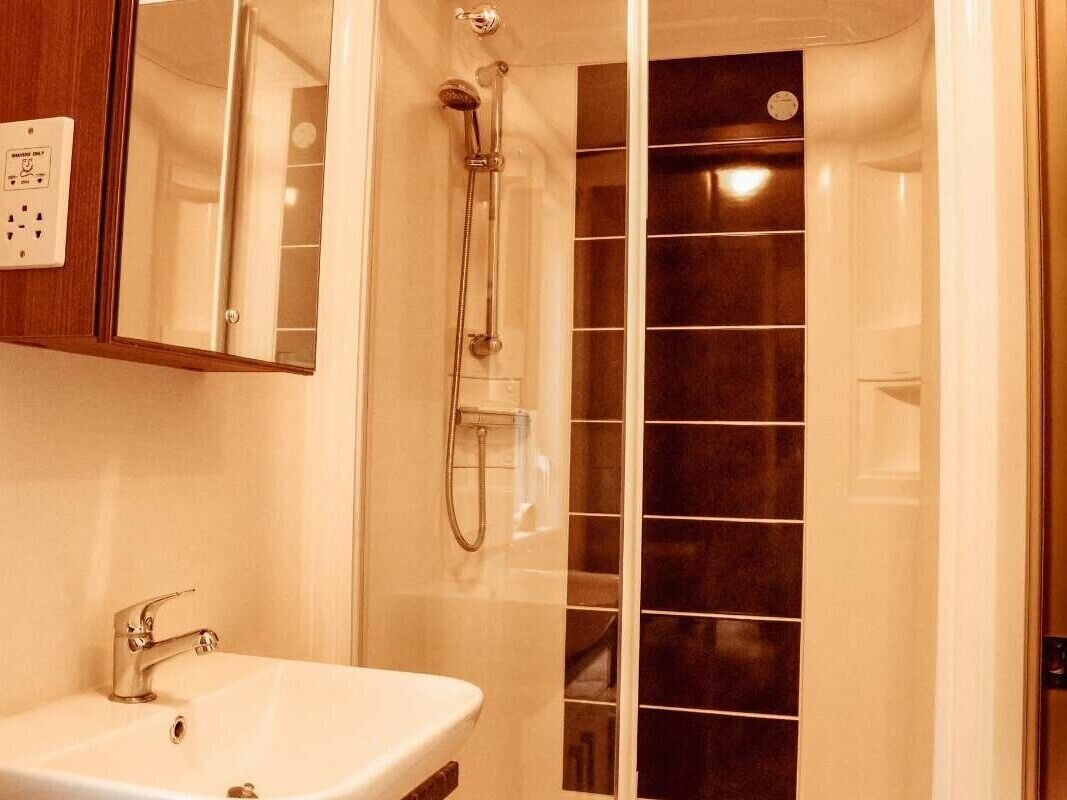 A bathroom with a white sink, a mirror, and a shower with dark tiles.
