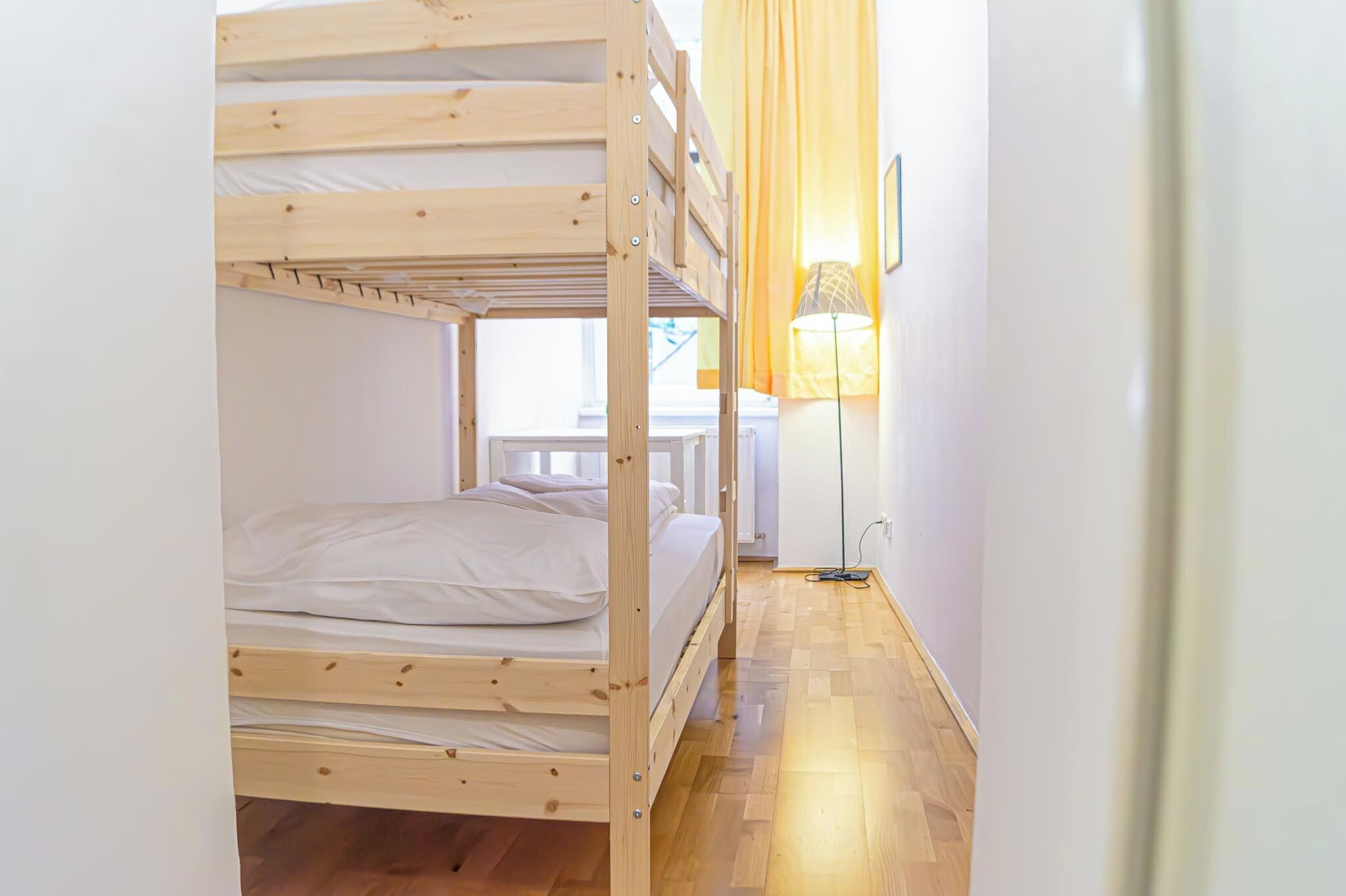 Habitación con literas, suelo de madera, lámpara y ventana con cortinas.