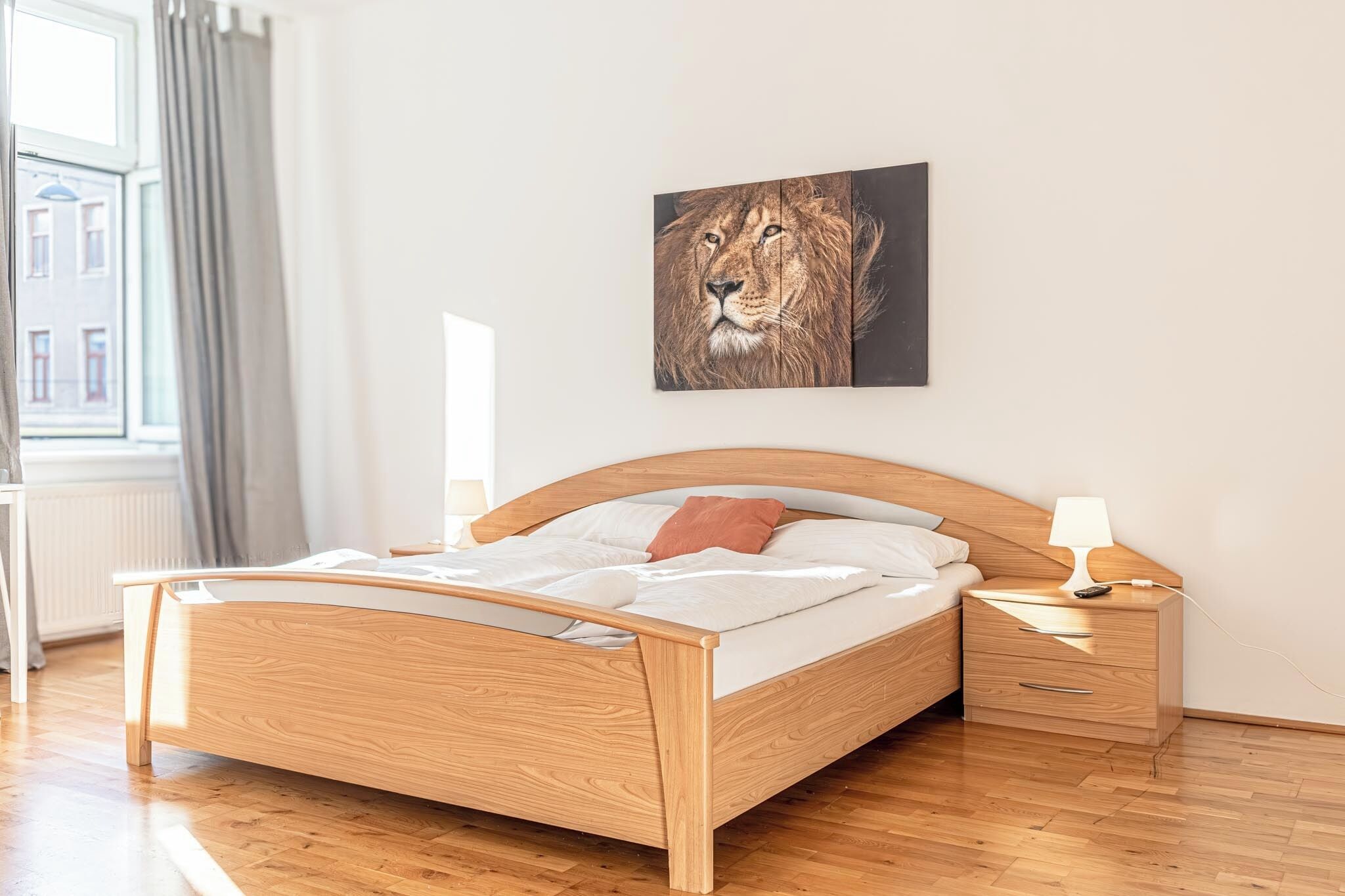 Ein hölzernes Bett mit Kopfteil, ein Nachttisch mit Lampe und ein Fenster mit Vorhängen.
