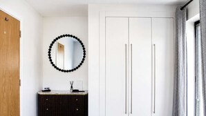 Une pièce avec une porte en bois, une coiffeuse noire et blanche, un miroir orné d’une guirlande de perles noires et une armoire blanche à deux portes.