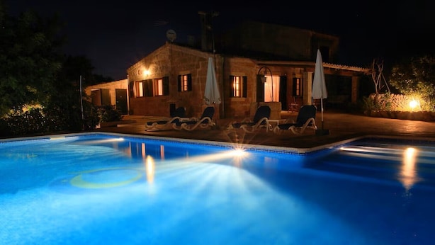A swimming pool with lounge chairs and umbrellas, surrounded by a building with multiple windows and a well-lit exterior. - Can Colau, rural experience in Mallorca, 4 bedrooms and swimming pool (Santa Margalida)
