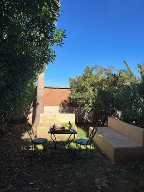 An outdoor seating area with a table and chairs, surrounded by greenery and a brick wall. - Villa Essalah & Spa - Entire Private Villa with Spa, Marrakech (Marrakech)