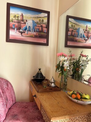 A room with a wooden desk, a mirror, a painting of a Moroccan scene, a pink patterned sofa, a tray with a teapot, glasses, and a bowl of fruit. - Villa Essalah & Spa - Entire Private Villa with Spa, Marrakech (Marrakech)