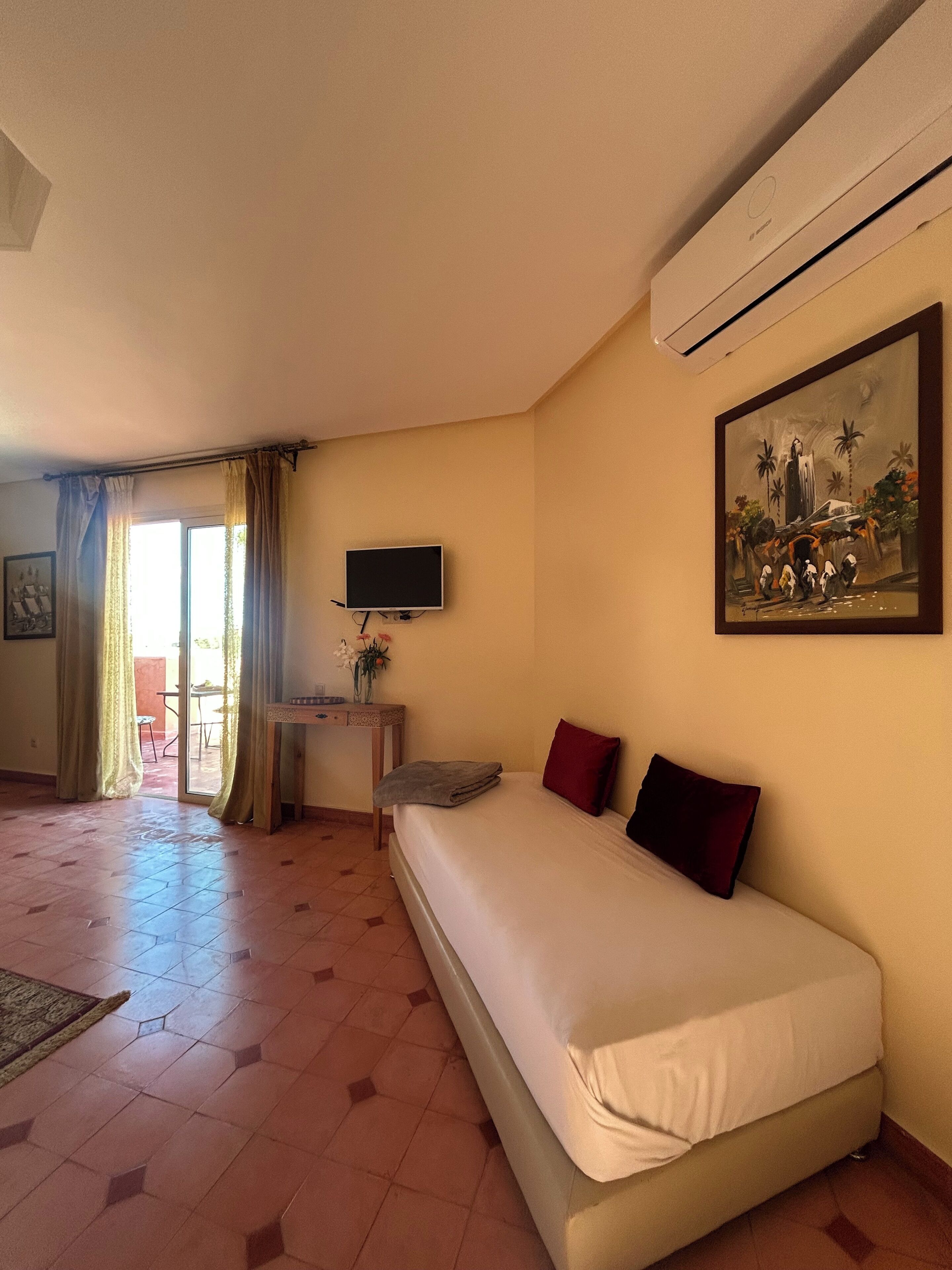Une chambre d’hôtel avec un lit, une télévision, un tableau et un bureau agrémenté d’un vase de fleurs.