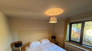 A hotel room with a bed, two bedside tables, a lamp, a window with a view, and a radiator. - Croydon Lodge (Minehead)