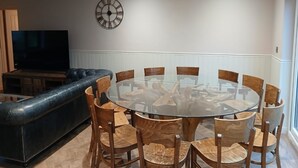 A modern living room with a glass-top dining table surrounded by wooden chairs, a black leather sofa, and a mounted wall clock. - Croydon Lodge (Minehead)