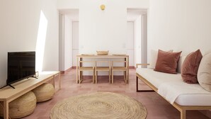 Een moderne woonkamer met een flatscreen televisie, een houten tafel met een mand, een geweven vloerkleed en een witte bank met bruine kussens.