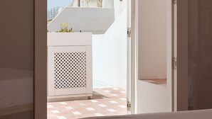Een slaapkamer met een bed, een open deur die leidt naar een balkon met uitzicht op gebouwen en een betegelde vloer.