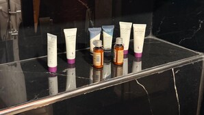 Una encimera de baño con diversos artículos de aseo, incluyendo tubos de loción corporal y una botella pequeña.