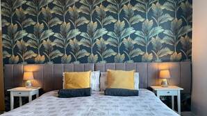 A double bed with a floral bedspread, two bedside tables with lamps, and a dark wallpaper with a leaf pattern. - Between the Beach and the Shops (Portsmouth)