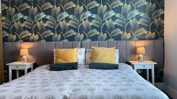 A double bed with a floral bedspread, two bedside tables with lamps, and a dark wallpaper with a leaf pattern.