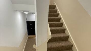 A carpeted staircase with a handrail, white walls, and a light fixture on the ceiling.