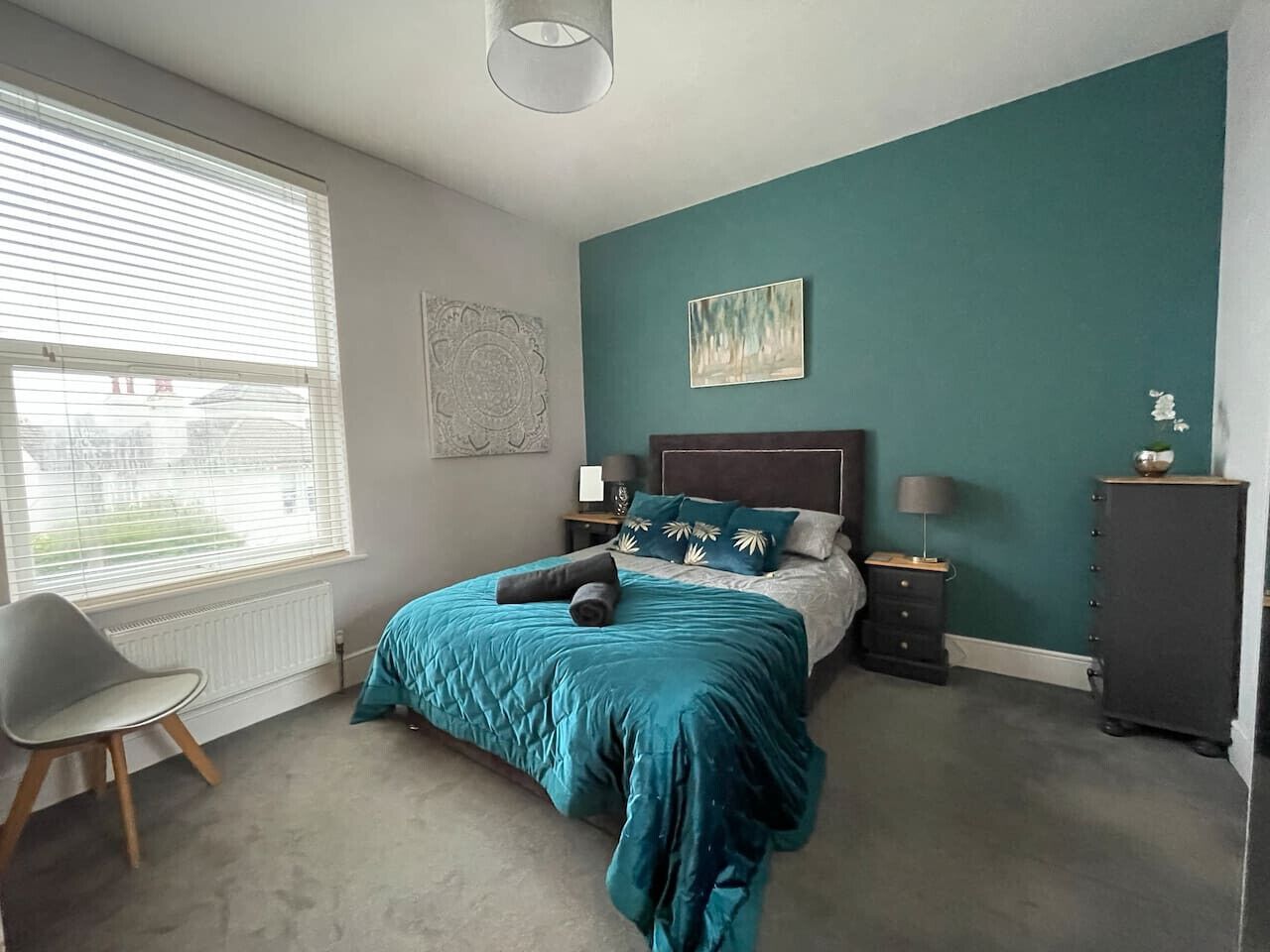A bedroom with a bed, bedside tables, a chair, and a radiator.