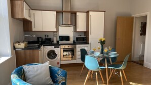 A compact kitchen with a washing machine, oven, and microwave. There is a dining area with a table and chairs. - Between the Beach and the Shops (Portsmouth)