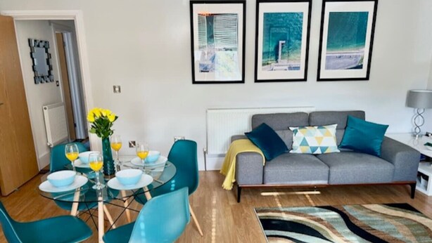A modern living room with a grey sofa, teal chairs, a glass dining table, and a colorful rug. - Between the Beach and the Shops (Portsmouth)