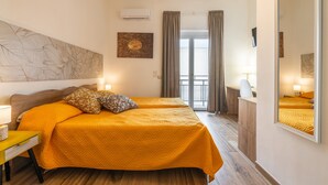 Ein Hotelzimmer mit zwei Betten, einem Schreibtisch, einem Stuhl, einem großen Spiegel und Blick auf einen Balkon.