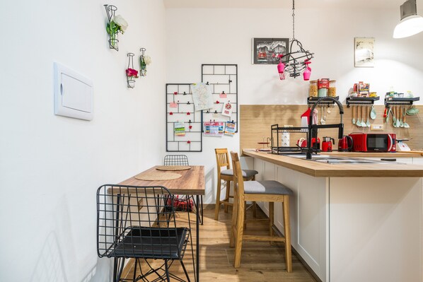Une cuisine compacte dotée d’un îlot central en bois, d’un coin repas avec une table et des chaises, ainsi que de divers ustensiles et appareils de cuisine.