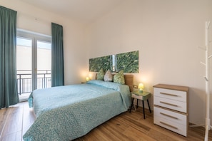 Une chambre à coucher avec un lit, une table de chevet, une commode, une fenêtre avec des rideaux et un tableau au mur.