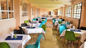Ein Restaurant mit mehreren Tischen und Stühlen, einer Küche im Hintergrund und großen Fenstern.