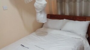 Ein ordentlich bezogenes Bett mit weißen Leinen, einem hölzernen Kopfteil und einem dekorativen Baldachin.