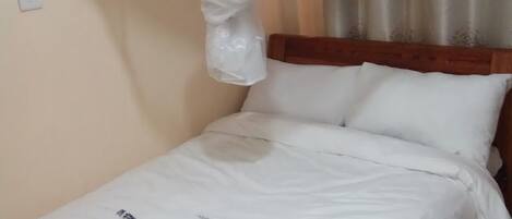 A neatly made bed with white linens, a wooden headboard, and a decorative canopy.
