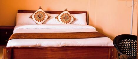 Habitación de hotel con una cama de madera, dos almohadones decorativos, un televisor en la pared y una silla.
