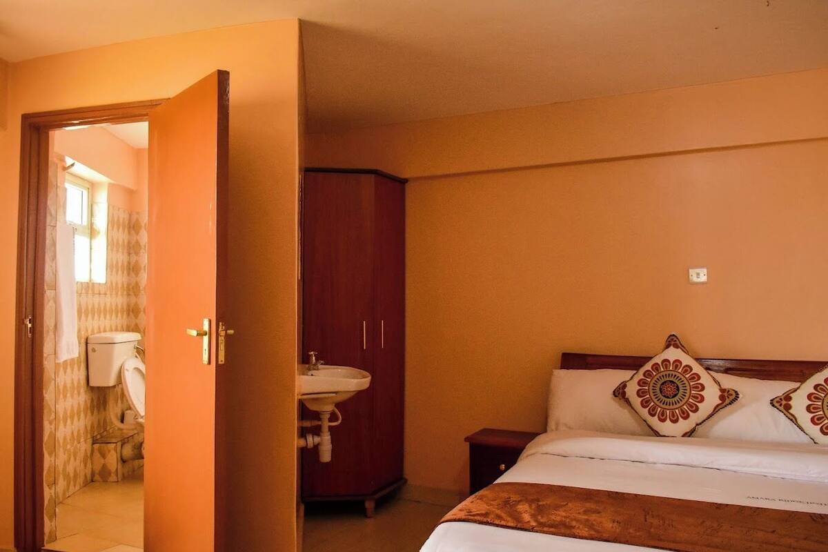 Ein Schlafzimmer mit einem Bett, einem Holzschrank, einem Nachttisch und einem durchgegangenen Tür sichtbaren Badezimmer.