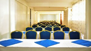 Ein Konferenzraum mit Tischen und Stühlen, ein langer Gang und eine Tür am Ende.