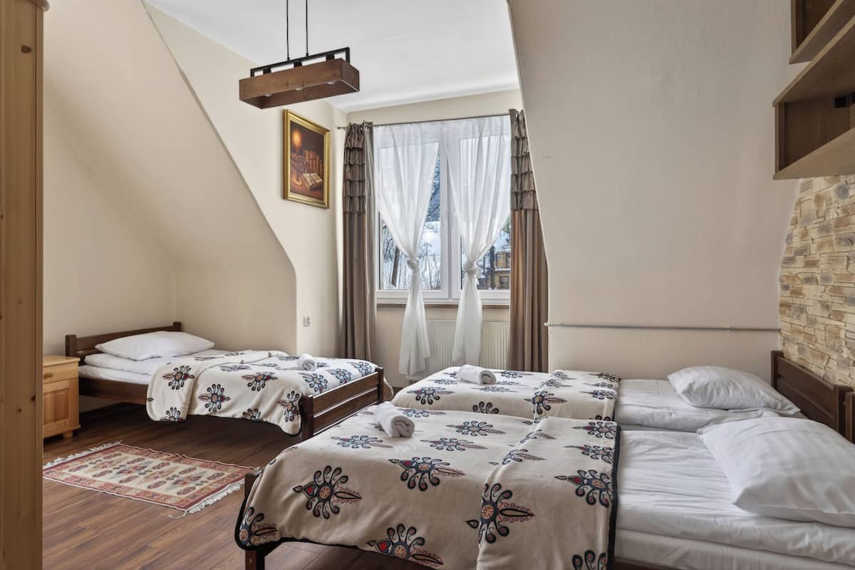 A bedroom with two beds, a wooden dresser, a window with curtains, and a hanging light fixture.