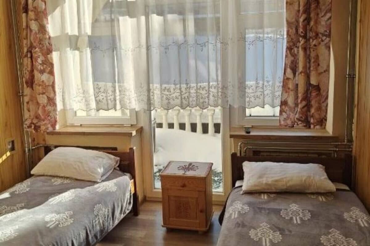 A bedroom with two beds, a wooden nightstand, and a window with sheer curtains.