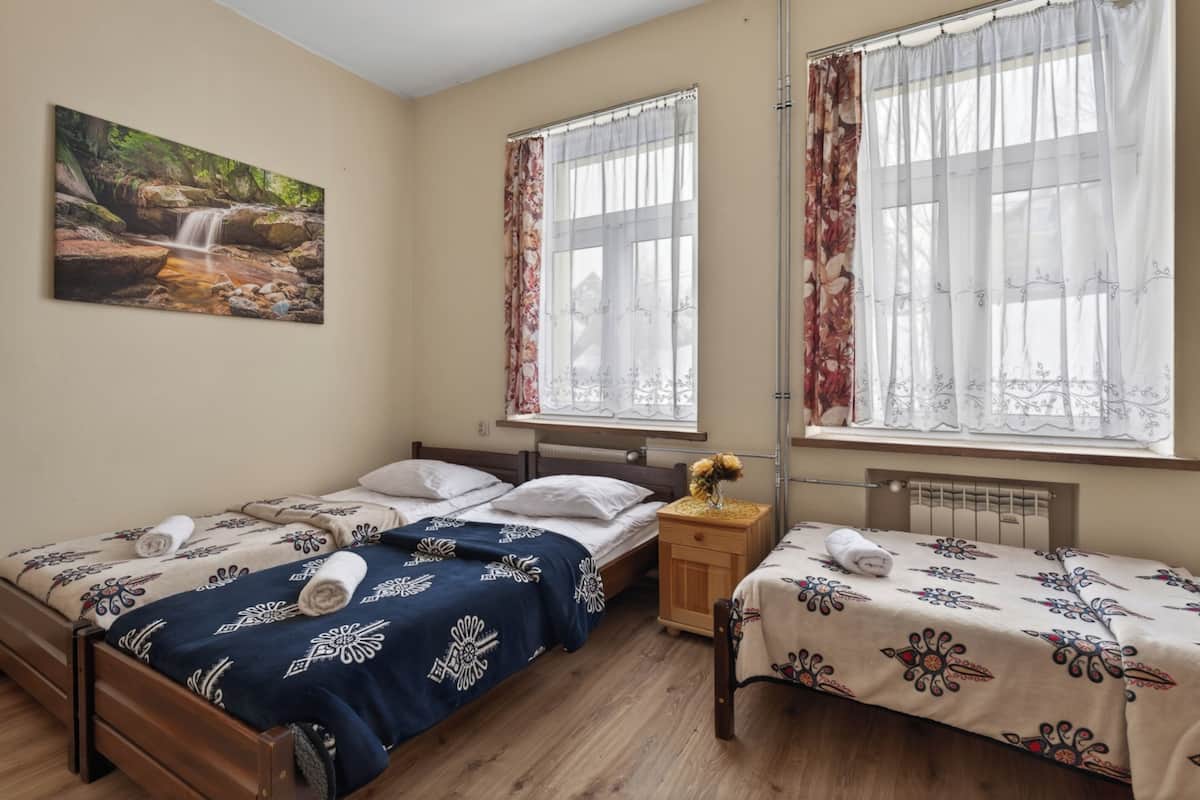 A room with two beds, a wooden floor, a painting of a waterfall, and a window with curtains.