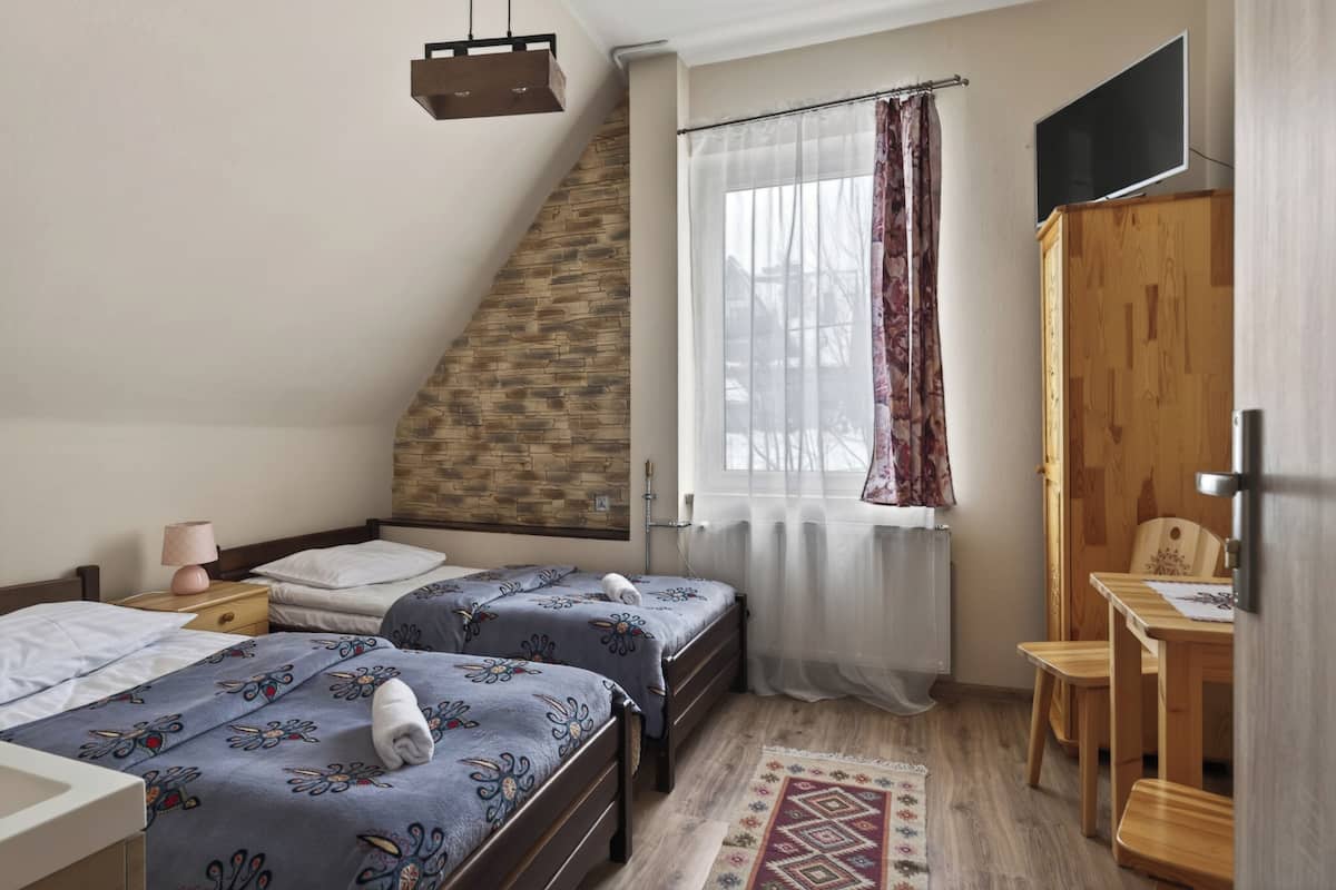 A bedroom with two beds, a wooden wardrobe, a desk, and a window with curtains.