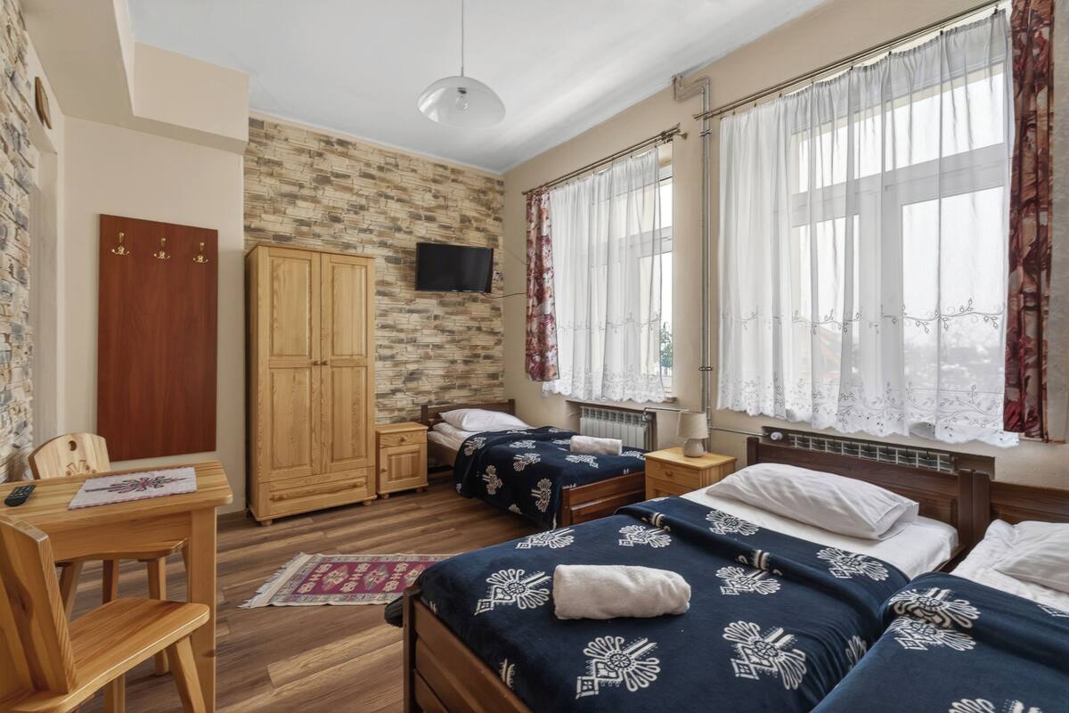 A bedroom with two beds, a wooden wardrobe, a television, and a desk with a chair.