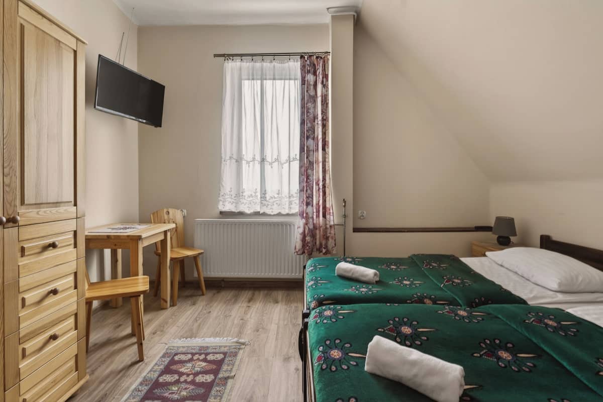 A bedroom with a bed, a desk, a chair, a television, and a window with curtains.