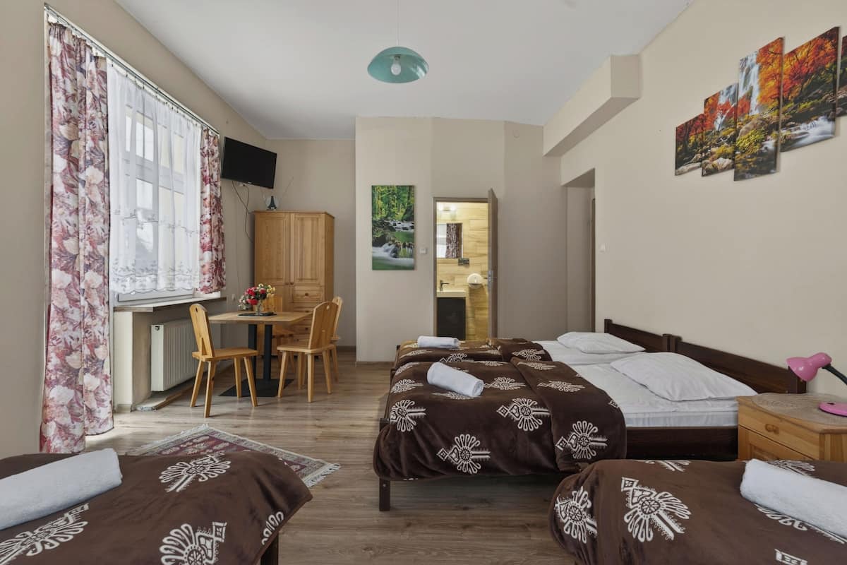 A hotel room with two beds, a desk, a chair, a TV, and a painting on the wall.
