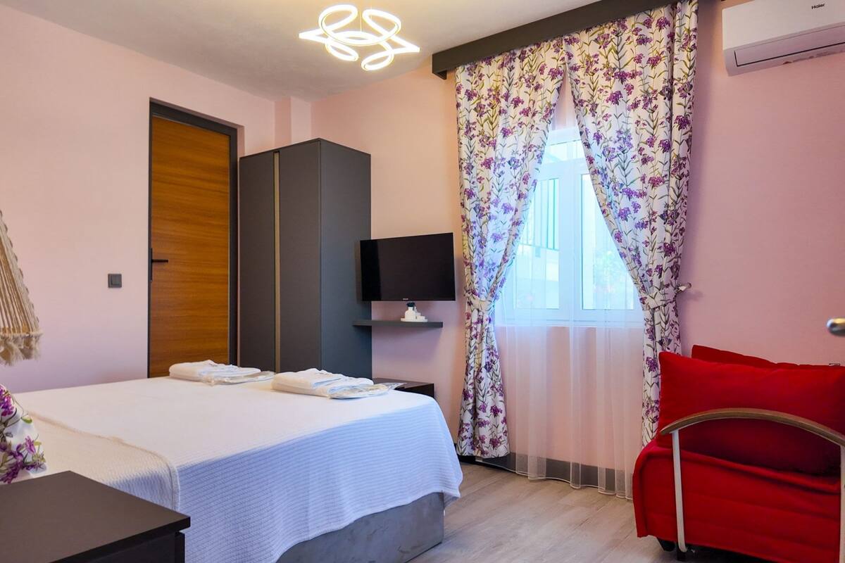 A hotel room with a bed, a TV, a desk, a lamp, and a red chair.