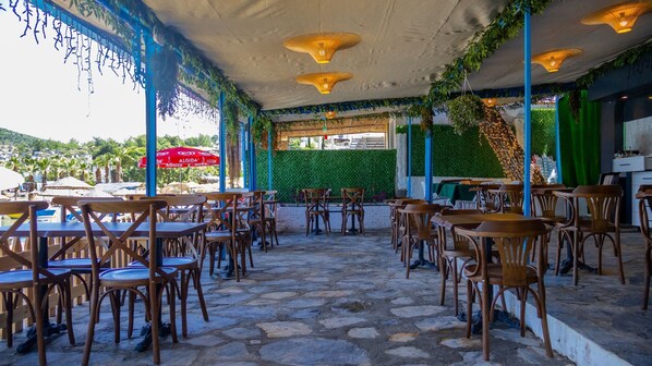 Un café en plein air avec un sol en pierre, des tables et des chaises en bois, et un mur végétal.