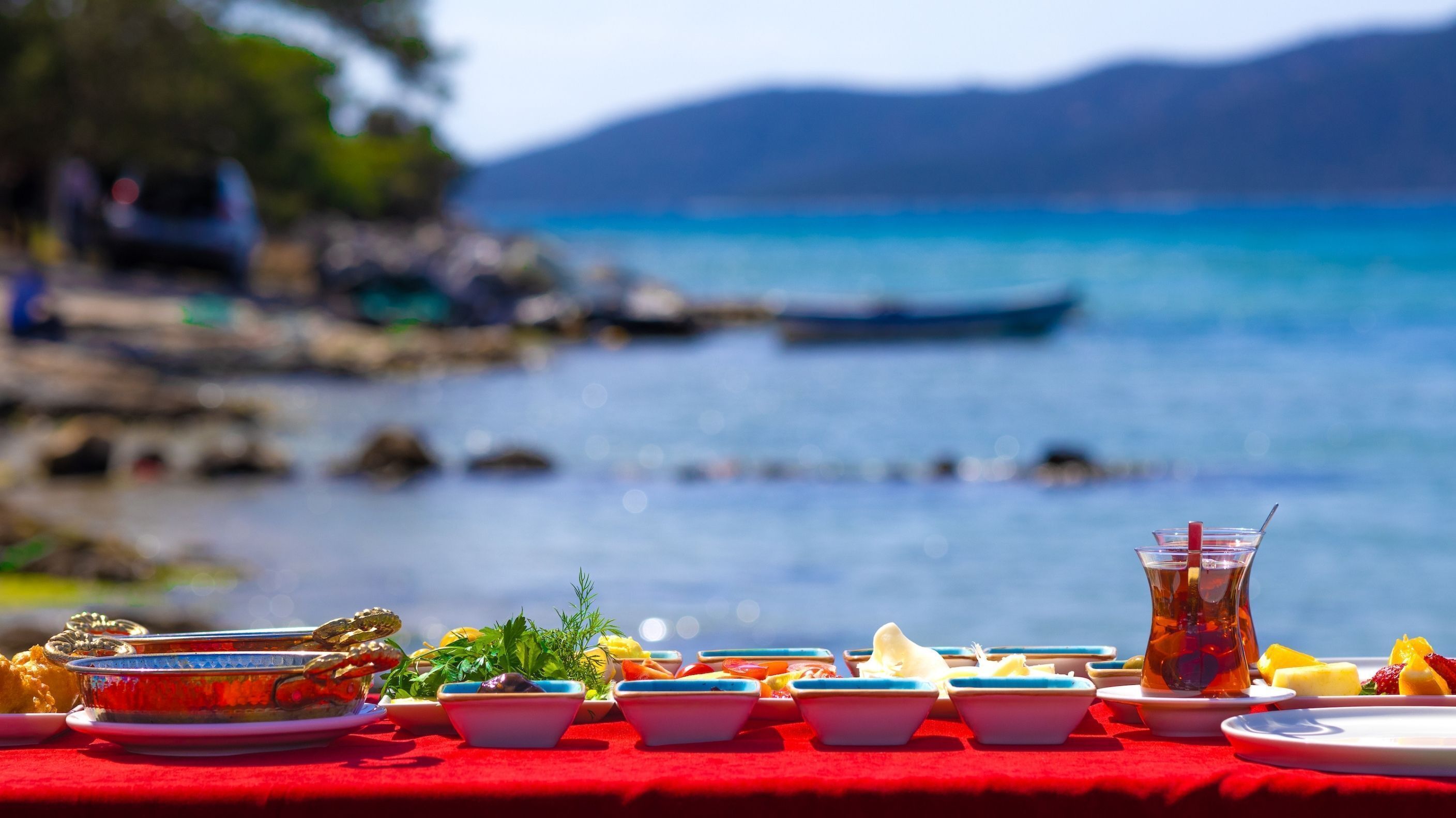 A table set with various dishes and a drink, overlooking a body of water with boats in the background.