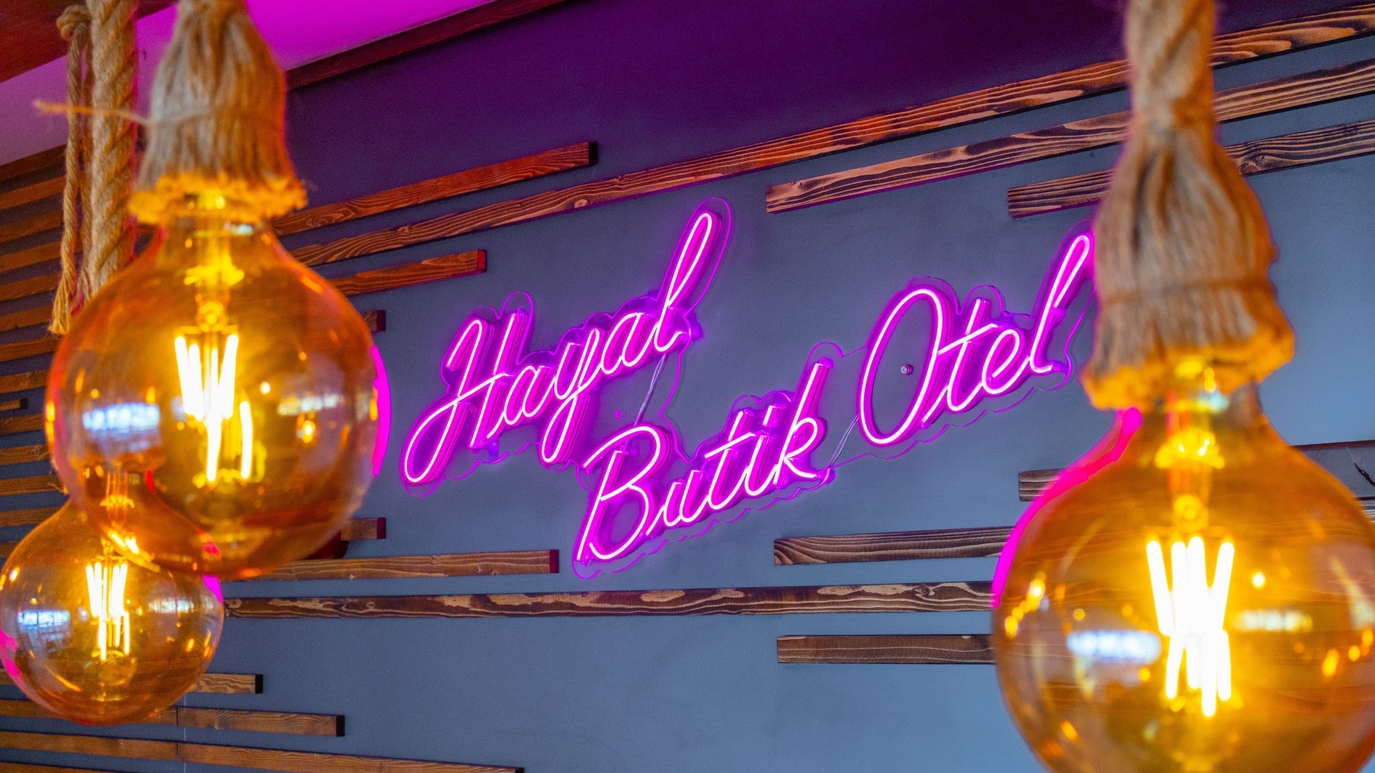 Letrero de neón con el texto 'Hoyal Butik Otel' sobre una pared azul con listones de madera.
