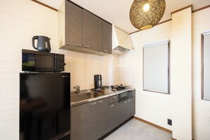 A modern kitchen with a black refrigerator, microwave, and kettle, a sink, and a stove. - STAY GATE Nishi-shinjuku gochome.57 ㎡ private hotel. 4min train to Shinjuku Sta. (shibuyaku honmachi)