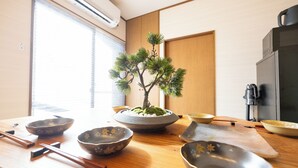 Et traditionelt japansk rum med tatamigulv, et bonsaitræ som midtpunkt, samt et tekøkken med køleskab og komfur.