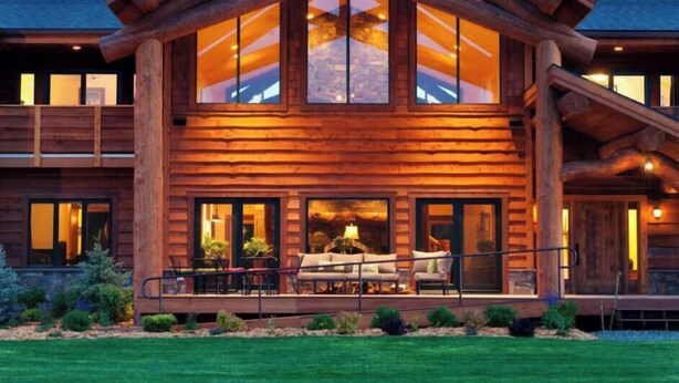 A large log cabin with a spacious porch and multiple windows.