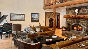 A spacious living room with a grand piano, leather sofas, a fireplace, and a wooden staircase.