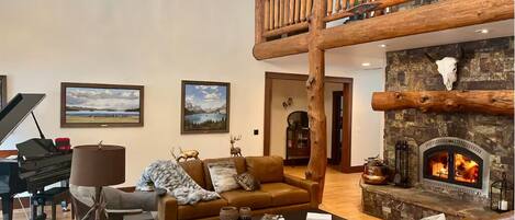 A spacious living room with a grand piano, leather sofas, a fireplace, and a wooden staircase.