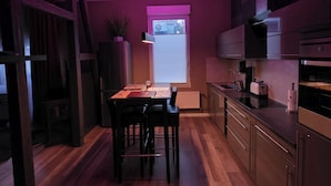 A modern kitchen with wooden flooring, a dining table with chairs, a refrigerator, a built-in oven, and a window with blinds. - Golden Dream The romantic apartment for erotic hours for two (REmscheid)