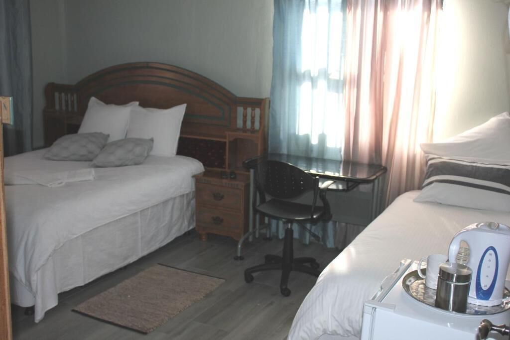 Ein Hotelzimmer mit Doppelbett, Schreibtisch mit Stuhl, einem kleinen Schminktisch und einem Nachttisch mit Wasserkocher und Tassen.