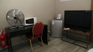 A compact room with a desk, a microwave, a small refrigerator, a TV, a fan, and a red chair. - Coco Palm B&B (Windhoek)